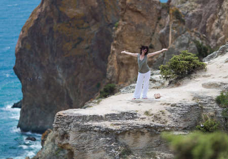 Middle age woman at the sea. Brunette woman in white trousers posing on cliff with arms outstretchedの写真素材