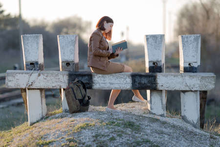 Railroad cul-de-sac on the outskirts of the city. Girl sitting on barrier and reading book in evening timeの写真素材