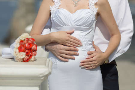 Hands of newly wedded after wedding ceremony. Hands of groom and bride with wedding rings on stomach...