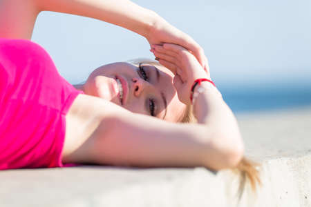 Waist up portrait of young woman in pink blouse with shadow on face. Attractive young woman lying on back and hiding her eyes from sunlight under her handsの写真素材