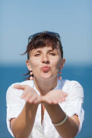 Portrait of middle aged woman against sea. Girl in white blouse sends an air kiss by both handsの写真素材