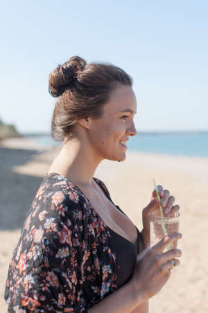 Girl on seashore. Attractive girl in robe holds glass of water and looking awayの写真素材