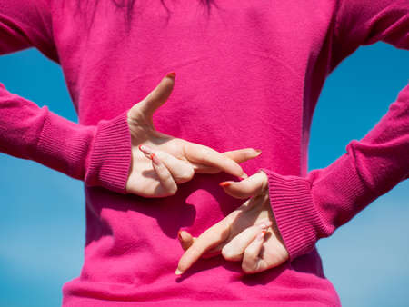 Hands of female person in pink blouse. Girl crossed her fingers and hiding hands behind backの写真素材