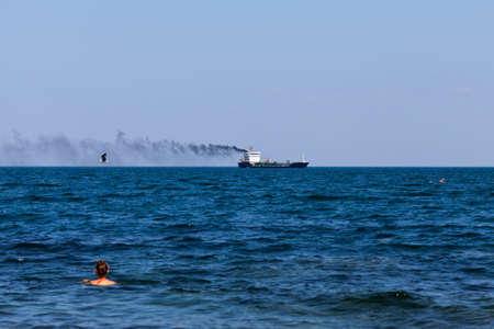 Seascape with a smoking ship. Black sea, swimming girl and seabird in windy dayの写真素材