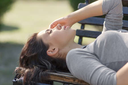Late-teens girl at the park. Eighteen-year-old girl lying on back on a bench in the park with eyes...