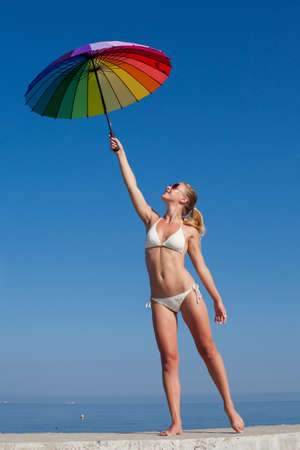 Portrait of girl under rainbow parasol. Attractive young woman holds multi colored umbrella over selfの写真素材