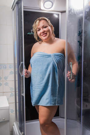 Portrait of girl in bathroom. Overweight woman wrapped in a towel with wet hair poses in a shower stall looking at camera smilingの写真素材