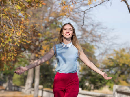 Portrait of female person in red suit outdoors. Young woman walks in autumn park with arms outstretchedの写真素材