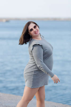 Expectant mother on seafront. Pregnant woman in gray dress and sunglasses walks along sea