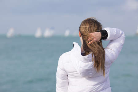 Late teen girl observing yacht regatta in windy day. Young female person stands on seashore and...