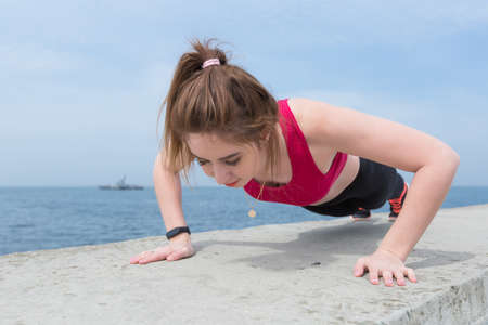 Sporty girl doing push-ups outdoors. Young woman in sportswear training on open air