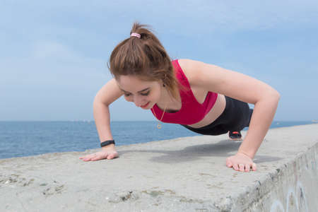 Sporty girl doing push-ups outdoors. Young woman in sportswear training on open airの写真素材