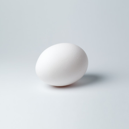 White chicken egg on white background with shallow depth of field closeupの写真素材
