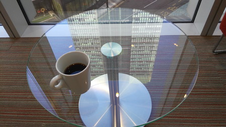 A cup of coffee on a glass table reflecting a skyscraper in Canary Wharf, London.のeditorial素材