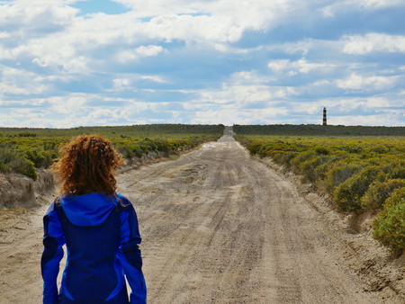 Scenic gravel road in the steppe of Patagonia near Punta Ninfas lighthouse, Puerto Madryn Argentina. Young female standing.の写真素材