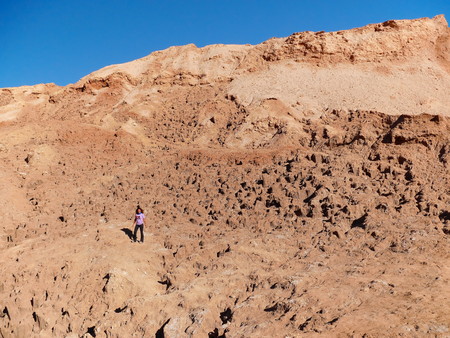 Young adult tourist at the incredible red rocks of the Moon Valley (Valle de la luna) near San Pedro De Atacama at sunset, with andean volcano Licancabur in the distance. Atacama desert is known as the driest place on earth.の写真素材