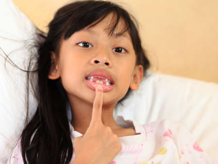 beautiful little girl grinning at the camera showing off her missing front tooth, close up portrait.