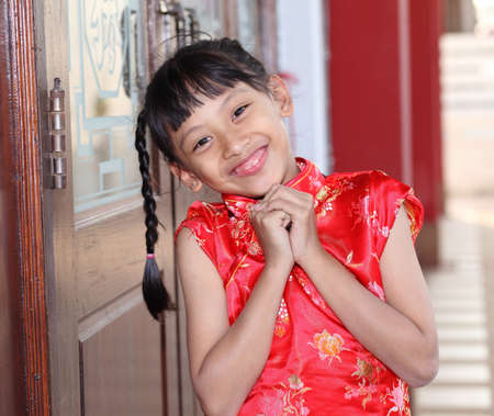 Cute lovely sweet asian chinese kid girl with smiling face on the temple.Little oriental girl wishing you a happy Chinese New Year.の写真素材