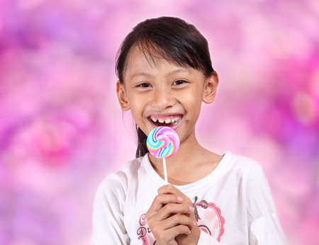 Beautiful little girl with lollipop on pink bokeh background.