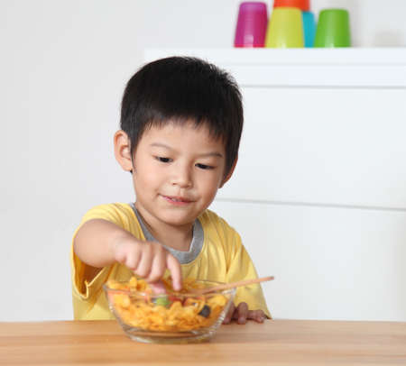 Little asian boy eating breakfast on wooden table in home.