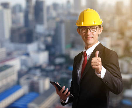 Businessman engineer hat make signal by thumb on blur city background.Engineering industrial industry businessman hand holding taplet.の写真素材