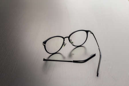 Old black glasses with broken legs against gray background.の写真素材