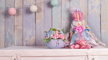 doll Tilda handmade on a blue background with a vase of flowers.の写真素材