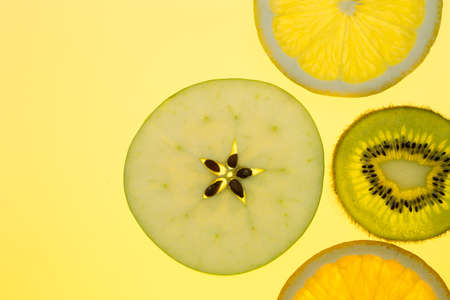 four orange apple and kiwi slices on yellow backgroundの写真素材