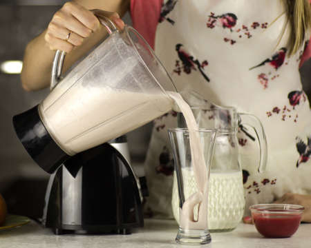 A beautiful woman preparing a milk cocktail with fruits in the kitchen.の写真素材
