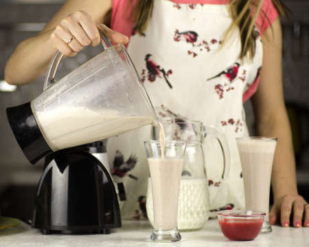 A beautiful woman preparing a milk cocktail with fruits in the kitchen.の写真素材