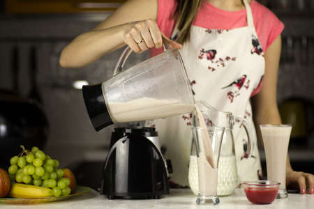 A beautiful woman preparing a milk cocktail with fruits in the kitchen.の写真素材