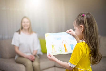 Child daughter congratulates mom and gives her painting. Mum and girl smiling and hugging. Family holiday and happiness. Happy mother's day!の写真素材