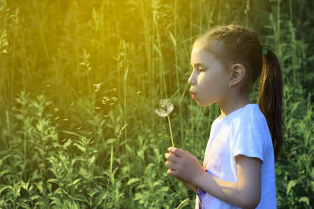 Beautiful child blowing away dandelion flower in spring. Fun on meadow.の写真素材