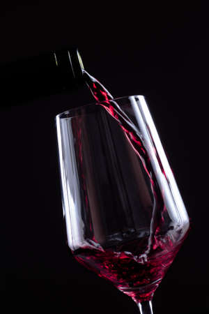 Red wine pouring in wineglass from a bottle on black background. Wine list design menu with copyspace. Alcohol beverage card backdrop.の写真素材