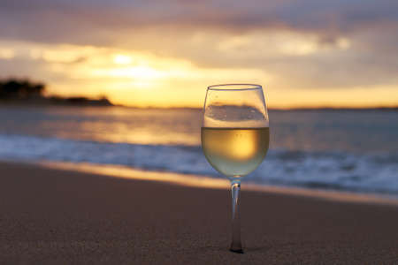 A glass  of white wine on the beach at sunset. Travel vacations concept.の写真素材