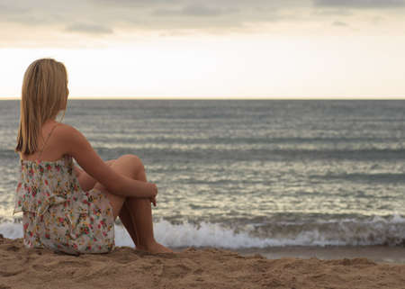 Young woman sitting on sand and looking to a sea. Travel vacations concept.の写真素材