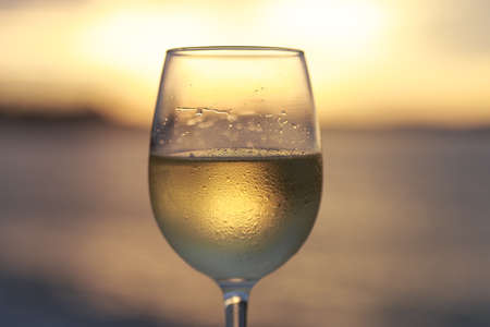 Wineglass of white wine at sunset dramatic sky background. Closeup. Travel vacations concept.の写真素材