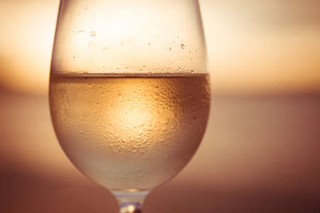 Wineglass of white wine at sunset dramatic sky background. Closeup. Travel vacations concept.の写真素材