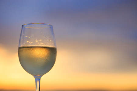 Wineglass of white wine at sunset dramatic sky background. Closeup. Travel vacations concept.の写真素材
