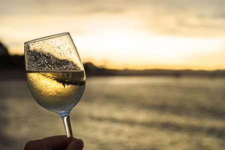 Female hand with a glass of white wine on the background of a beautiful sunset.  Travel vacations concept.の写真素材