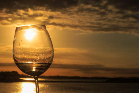 Female hand with a glass of white wine on the background of a beautiful sunset.  Travel vacations concept.の写真素材