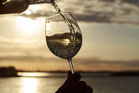 Female hand with a glass of white wine on the background of a beautiful sunset.  Travel vacations concept.の写真素材