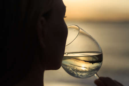 Closeup young beautiful woman is drinking white wine celebrating anniversary outdoors  at the  sea background.の写真素材