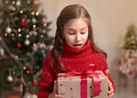 Cute little child girl with present gift box near Christmas tree at home. Happy Holiday and Merry Christmas.の写真素材