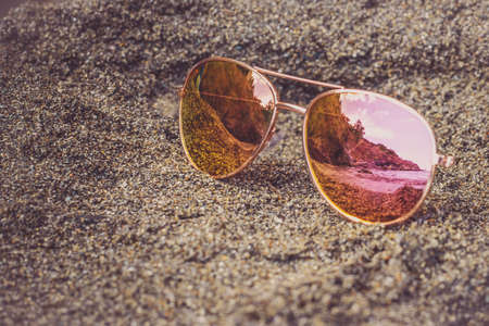 Sunglasses at the beach with sea reflection. Holidays, travel, vacation and happiness concept.の写真素材
