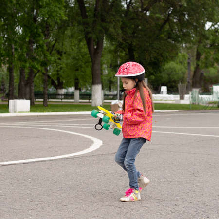 Cute little preteen girl wearing helmet riding on a skateboard in beautiful summer park