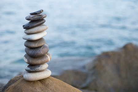 Stones pyramid on sand symbolizing zen, harmony, balance. Ocean at sunset in the background.の写真素材