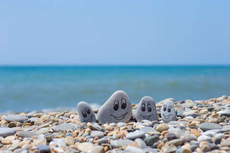 Group of stones with drawn faces in the sand. Father, mother, daughter and son. Concept of happy familyの写真素材