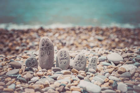 Pebbles with drawn faces in the sand. Father, mother, daughter and son. Family of cats vocation concept.の写真素材
