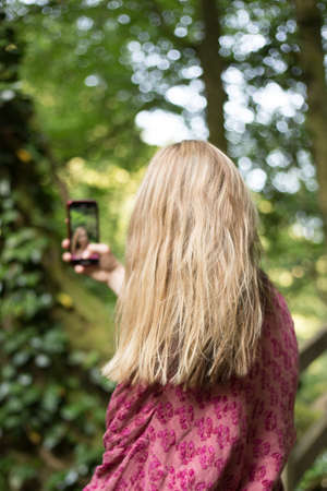 Woman taking pictures with smartphone in the forest.の写真素材